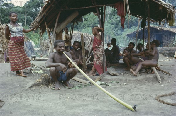 CONGO, Tribal Peoples, Pygmies in forest near Ituri.  Man in foreground smoking dried local leaves in long bamboo pipe.