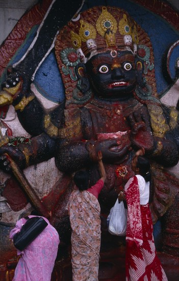 NEPAL,  , Kathmandu, Women making offerings at the Kala Bhairab or black Shiva in Durbar Square representing the fearsome Tantric form of Shiva in Nepal.