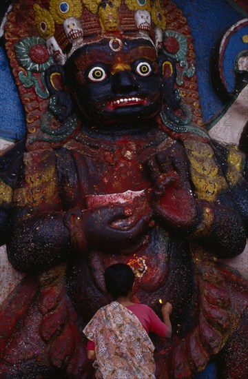 NEPAL,  , Kathmandu, Woman making offerings at the Kala Bhairab or black Shiva in Durbar Square representing the fearsome Tantric form of Shiva in Nepal.