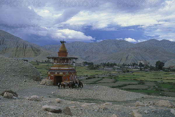 NEPAL, Mustang, Tsarang, Group of riders on ponies beside stupa marking the entrance to Tsarang.