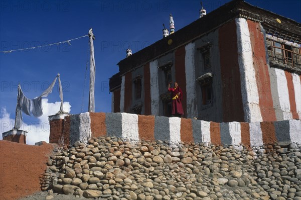 NEPAL, Mustang, Tsarang, Head monk looking out from terrace of temple painted with coloured stripes.