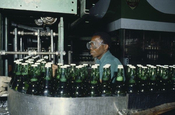 NIGERIA, Industry, Brewery with man wearing safety goggles working  behind machinery and green glass bottles.