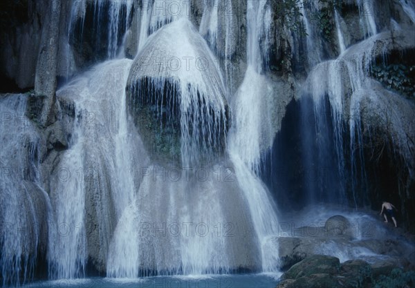 LAOS, Luang Prabang Prov., Kuang Si Falls, Close view of waterfall with man climbing rocks at side.