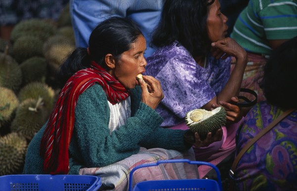 INDONESIA, Sumatra, Berastagni, Karo Batak woman eating durian fruit at market in town in the Karo Highlands.