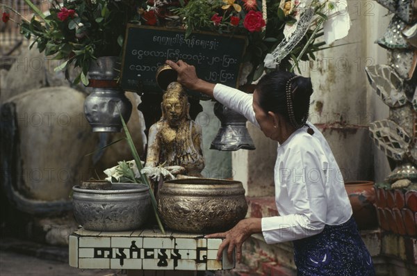 MYANMAR, Yangon, Woman making offering at shrine in the Shwedagon Pagoda.