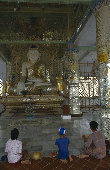 MYANMAR, Sagaing, Woman and children kneeling in front of giant seated Buddhist figure.