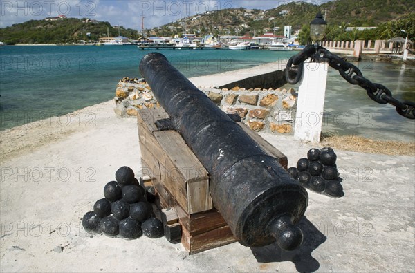 WEST INDIES, St Vincent & The Grenadines, Union Island, Ancient canon on the harbourside at Clifton with the town and mooring behind