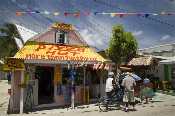 WEST INDIES, St Vincent & The Grenadines, Union Island, Men talking outside pizza restaurant and tourist shop in Clifton
