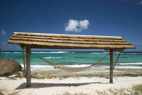 WEST INDIES, St Vincent & The Grenadines, Palm Island, Hammock under a shelter by the beach at Palm Island Resort