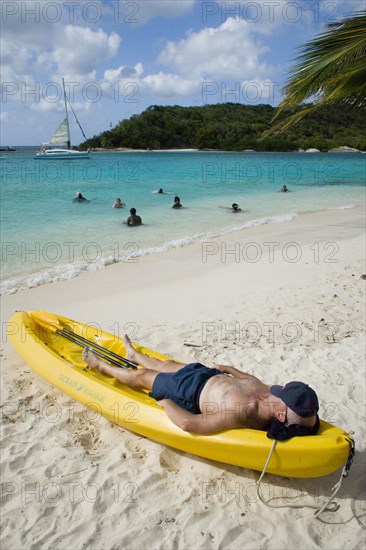 WEST INDIES, St Vincent & The Grenadines, Tobago Cays, Man lying in kayak sunbathing on the beach of Petit Bateau