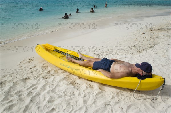 WEST INDIES, St Vincent & The Grenadines, Tobago Cays, Man lying in kayak sunbathing on the beach of Petit Bateau