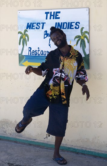 WEST INDIES, St Vincent & The Grenadines, Union Island, Man dancing beside a restaurant sign in Clifton