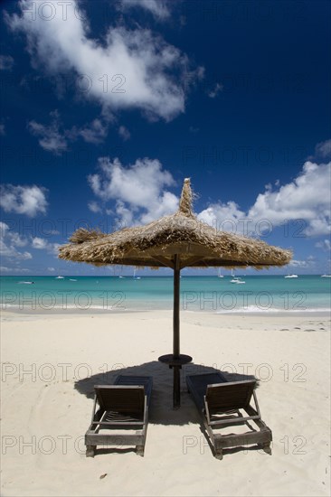 WEST INDIES, St Vincent & The Grenadines, Canouan, Palapa thatched shelter and sunbeds at Tamarind Beach Hotel in Charles Bay with moored yachts