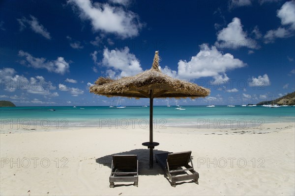 WEST INDIES, St Vincent & The Grenadines, Canouan, Palapa thatched shelter and sunbeds at Tamarind Beach Hotel in Charles Bay with moored yachts