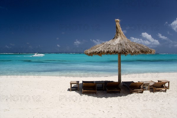 WEST INDIES, St Vincent & The Grenadines, Canouan, Palapa thatched shelter and sunbeds on Godahl Beach at Raffles Resort with speedboat passing along the bay