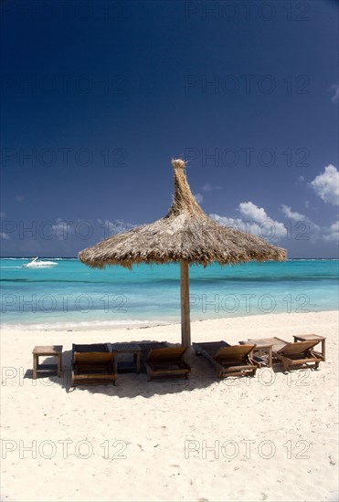 WEST INDIES, St Vincent & The Grenadines, Canouan, Palapa thatched shelter and sunbeds on Godahl Beach at Raffles Resort with speedboat passing along the bay