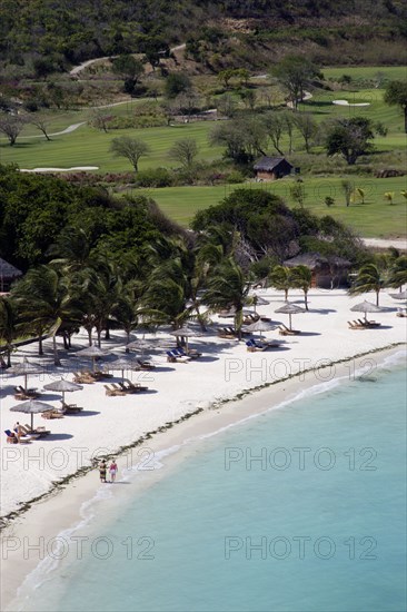 WEST INDIES, St Vincent & The Grenadines, Canouan, Two women walking along Jambu Beach at Raffles Resort with the Trump International Golf Course behind