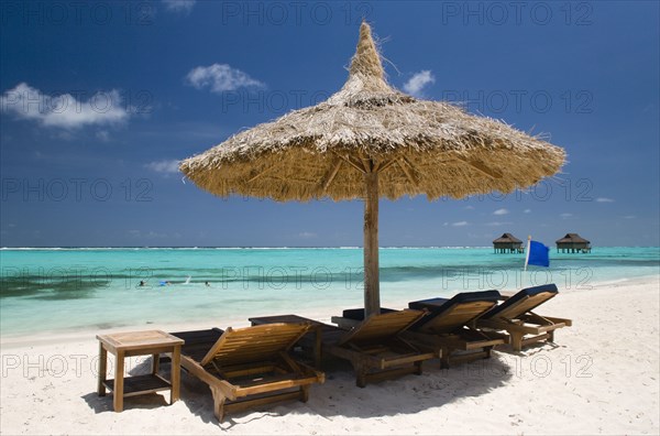 WEST INDIES, St Vincent & The Grenadines, Canouan, Palapa thatched shelter and sunbeds on Godahl Beach at Raffles Resort with offshore treatment rooms of the Amrita Spa beyond