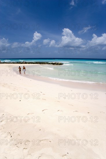 WEST INDIES, Barbados, Christ Church, Couple walking towards sea defences on Rockley Beach also known as Accra Beach after the hotel there