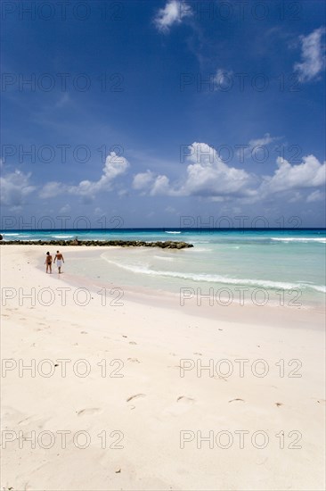 WEST INDIES, Barbados, Christ Church, Couple walking towards sea defences on Rockley Beach also known as Accra Beach after the hotel there