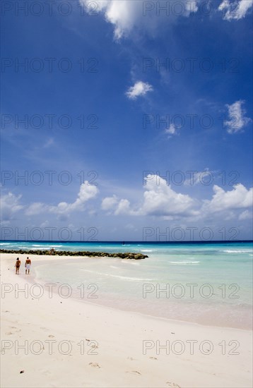 WEST INDIES, Barbados, Christ Church, Couple walking towards sea defences on Rockley Beach also known as Accra Beach after the hotel there