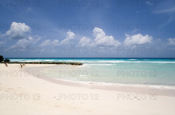 WEST INDIES, Barbados, Christ Church, Couple walking towards sea defences on Rockley Beach also known as Accra Beach after the hotel there