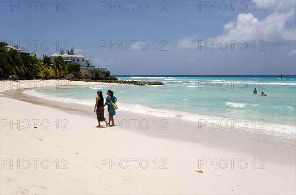 WEST INDIES, Barbados, Christ Church, Two women walking on the sand past a couple in the sea at Rockley Beach also known as Accra Beach after the hotel there