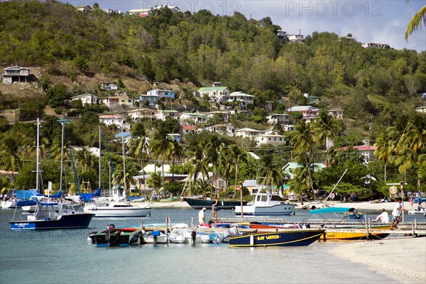 WEST INDIES, St Vincent & The Grenadines, Bequia, Jetty with moored yachts in Admiralty Bay with hillside houses beyond in Port Elizabeth