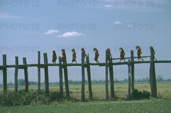 MYANMAR, People, Line of monks with fans crossing wooden bridge raised high above agricultural land.