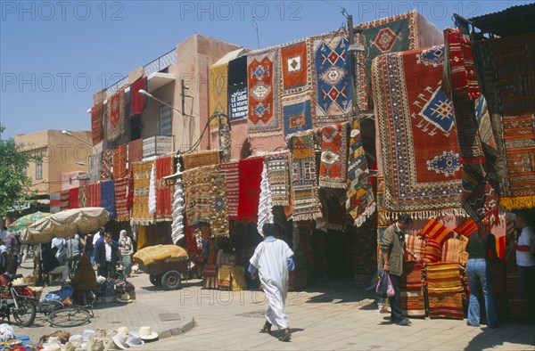 MOROCCO, Marrakesh, The souk with carpets displayed from walls and awnings of shopfronts opposite street vendors.