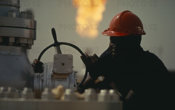 NIGERIA, Industry, Portrait of oil worker with flare of burnt off gas behind him.