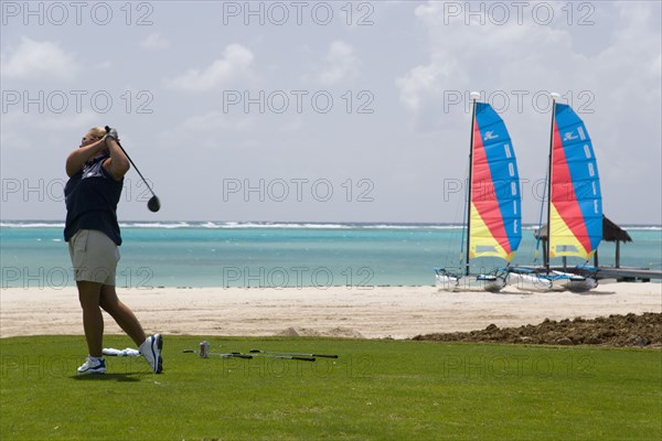 WEST INDIES, St Vincent & The Grenadines, Canouan, Lady golfer teeing off on the Raffles hotel practice range with beach and hobbie cats behind