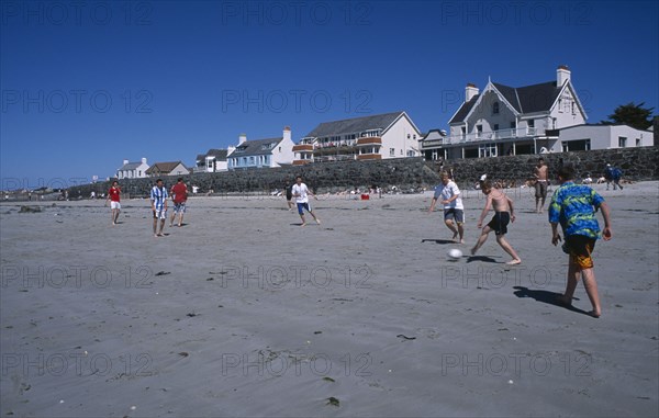 UNITED KINGDOM, Channel Islands, Guernsey, Castel. Cobo Bay. Young men playing football on sandy beach