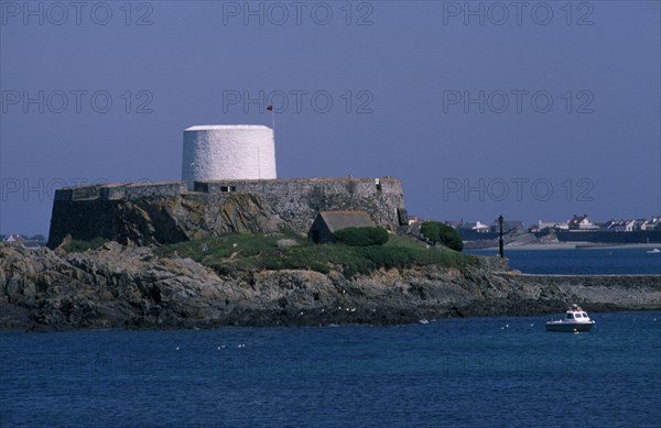 UNITED KINGDOM, Channel Islands, Guernsey, St Peters. Fort Grey and Shipwreck Museum. View across sea towards the white Martello Tower. Also known as the Chateau de Rocquaine or the Cup and Saucer.