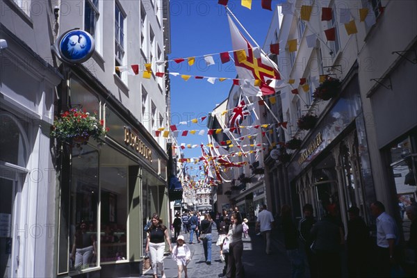 UNITED KINGDOM, "Channel Islands						", Guernsey, "St Peter Port. View up narrow cobbled High Street, pedestrian shopping street with colourful flags attached to buildings."
