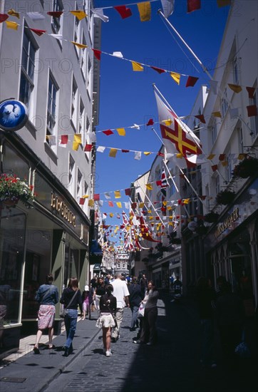UNITED KINGDOM, Channel Islands, Guernsey, "St Peter Port. View up narrow cobbled high street, pedestrian shopping street with colourful flags attached to buildings."