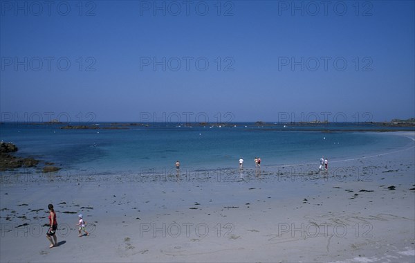 UNITED KINGDOM, Channel Islands, Guernsey, Castel. Cobo Bay. View across beach towards sea with people paddling and walking along the sand