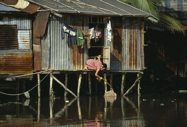 VIETNAM, South, Ho Chi Minh City, "Woman retrieving her washing from the Rach Thi Nghe backwater of the Saigon River, kneeling from doorway of tin hut built on wooden stilts."