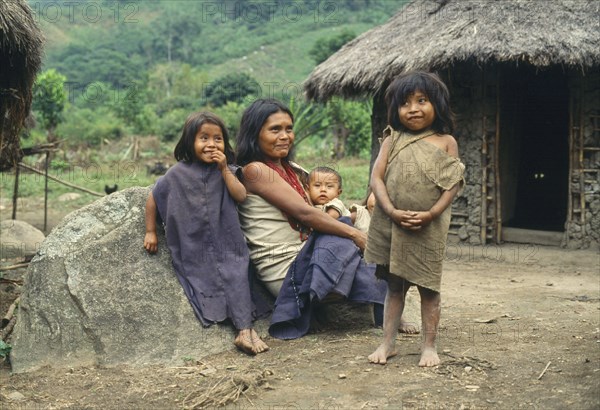 COLOMBIA, People, Kogi, Kogi woman sitting on the ground with three children outside their thatched home