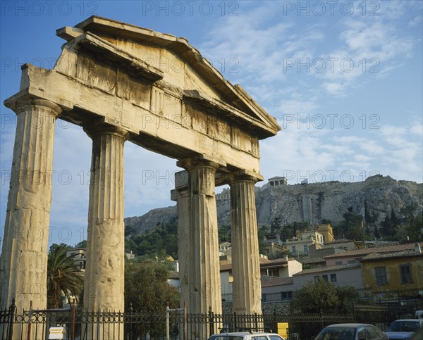 GREECE, Central, Athens, Plaka - Ancient Agora and Acropolis on top. Old ruined columns behind a fence with houses and a hill in the background.