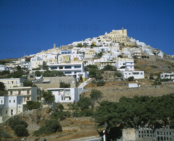 GREECE, Cyclades Islands, Syros, Ermoupolis. The Catholic quater of Ano Syros and church of Ag. Yiorgios. Houses covering mountain side with trees and a wall in the foreground.