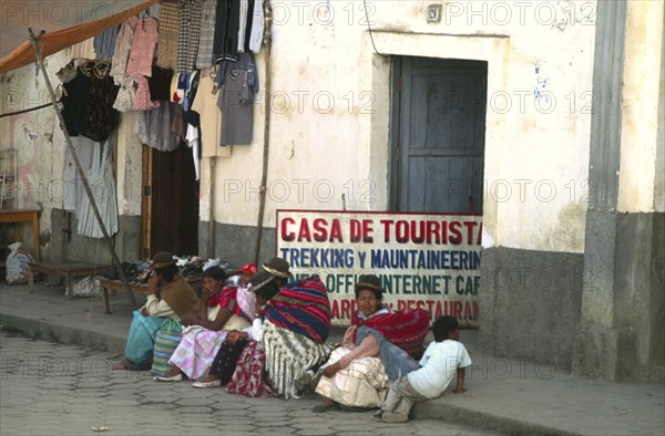 BOLIVIA, North, Sorata, Indigenous women and children sat on pavement outside trekkers agency internet cafe.