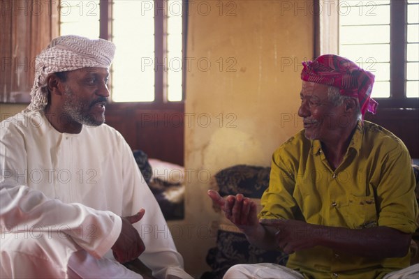 OMAN, Sur, "Discussioin between two Omanis, including traditional fisherman on the right hand side."