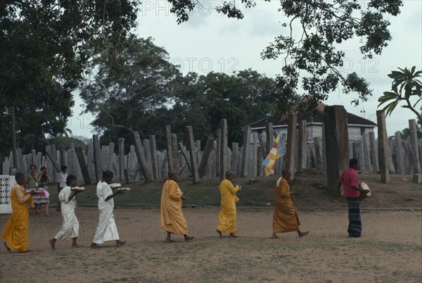 SRI LANKA, Anuradhapura, Buddhist monks and nuns carrying puja offerings past columns of the ruins of the Brazen Palace.