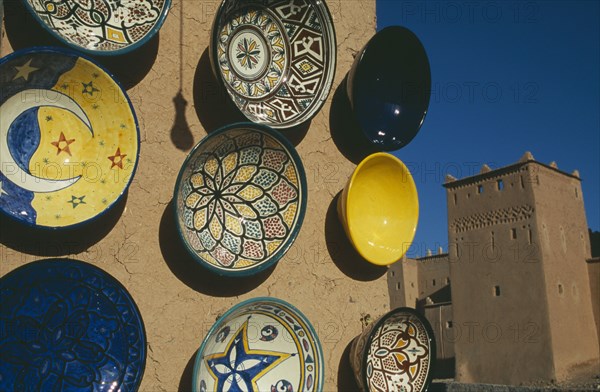 MOROCCO, Ouarzazate, Painted ceramic dishes displayed on wall with Kasbah Taorirt partly seen behind.