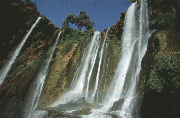 MOROCCO, Middle Atlas, Cascades d’Ouzoud, Waterfalls of the Olives.  Multiple falls cascading over rocks with sunlight through spray causing rainbow effect.