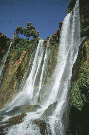 MOROCCO, Middle Atlas, Cascades d’Ouzoud, Waterfalls of the Olives.  Multiple falls cascading over rocks with sunlight through spray causing rainbow effect.