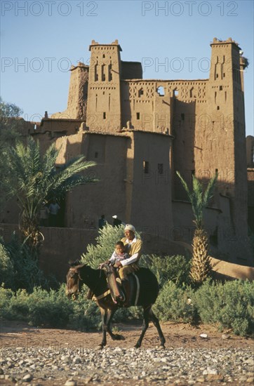MOROCCO, Ait Benhaddou, Kasbah used in films including Lawrence of Arabia and Jesus of Nazareth.  Exterior with passing man and boy riding mule in foreground.