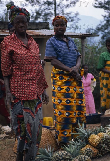 BURUNDI, Market, Fruit, "Women in bright dresses at side of road, standing beside their pineapples for sale."