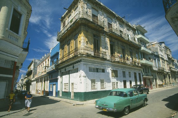 CUBA, Havana, Street corner with traditional buildings with overhanging balconies.  Turquoise car passing in the foreground.